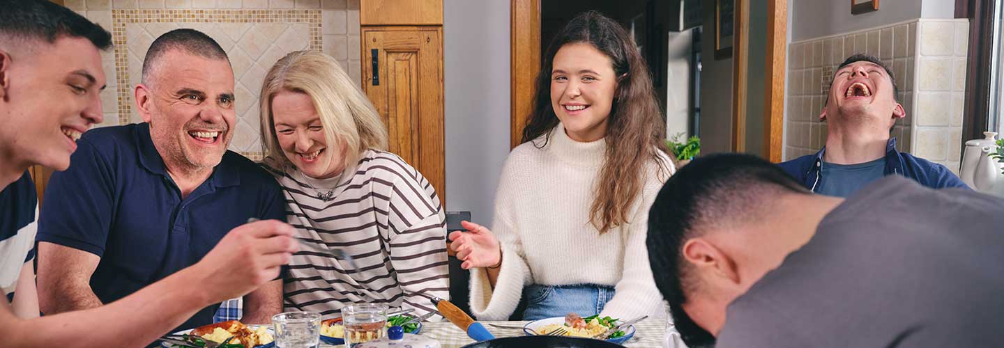 Mother, daughter and son laughing together with the wider family over breakfast