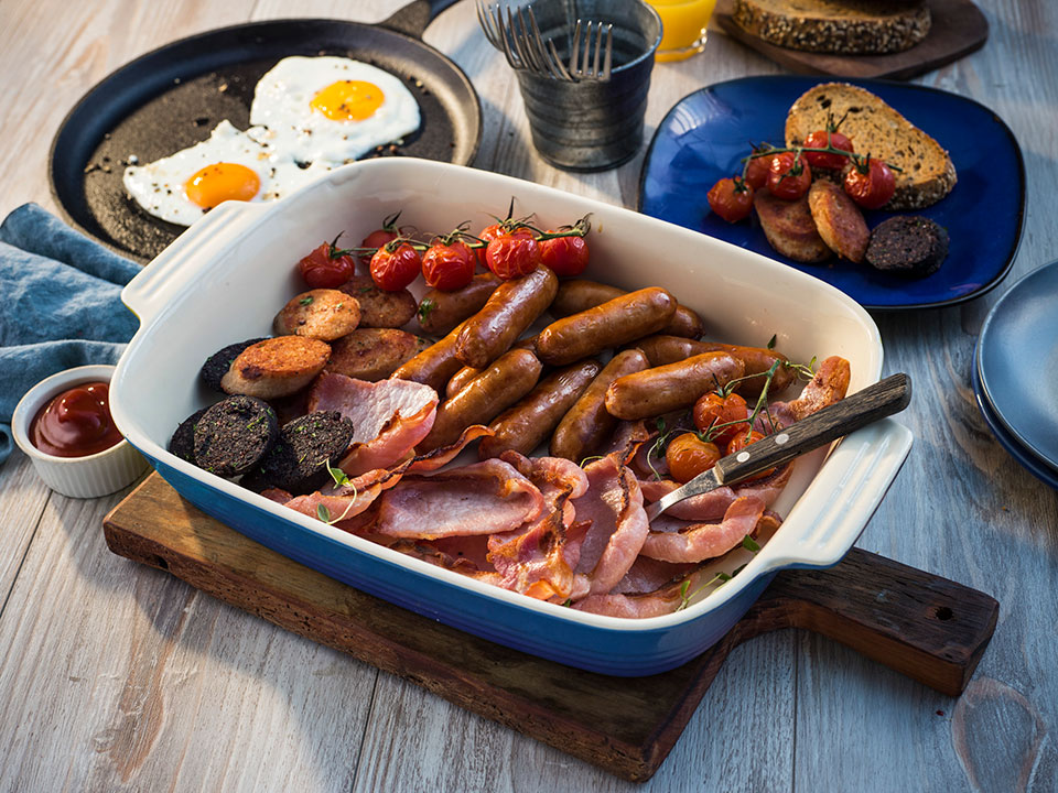 Oven dish filled with sausage, rasher, pudding and tomatoes